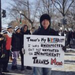 Marcher holding a "thanks mom" sign.