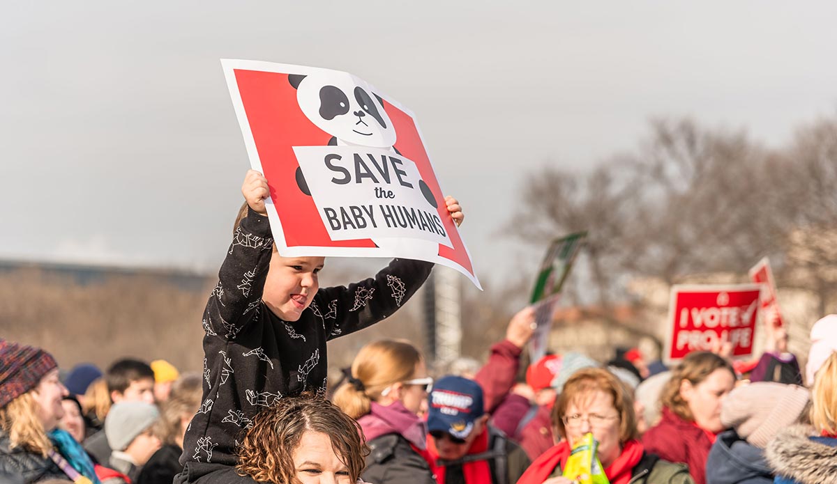 Image of a child holding a Save the Baby Humans sign on his parent's shoulders